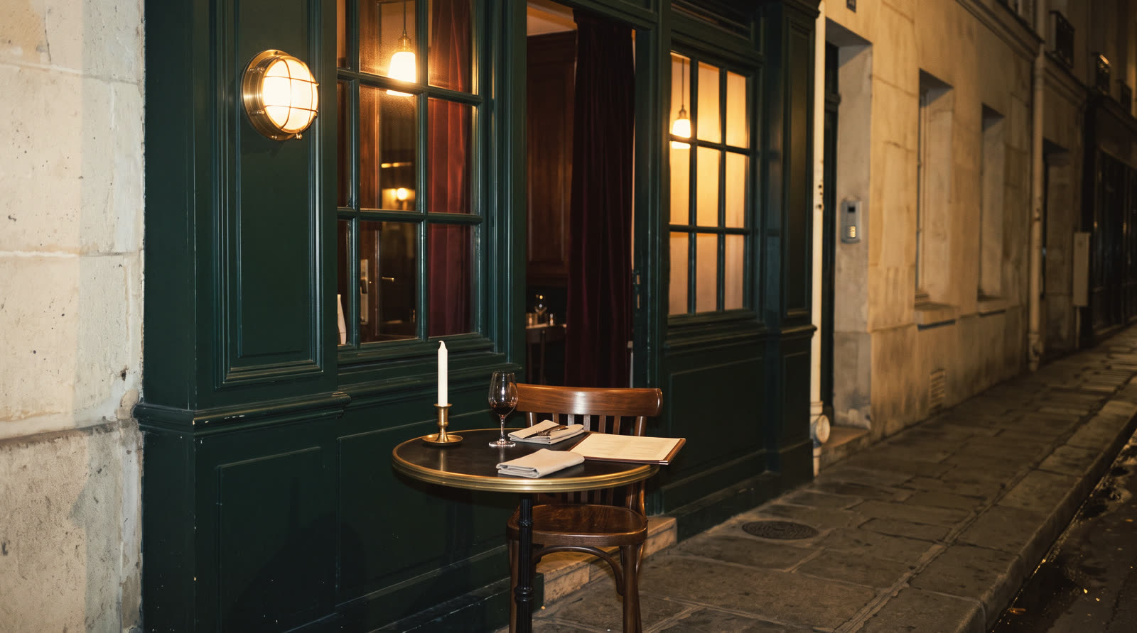 A small restaurant at night on a narrow limestone street, one table outside with a candle