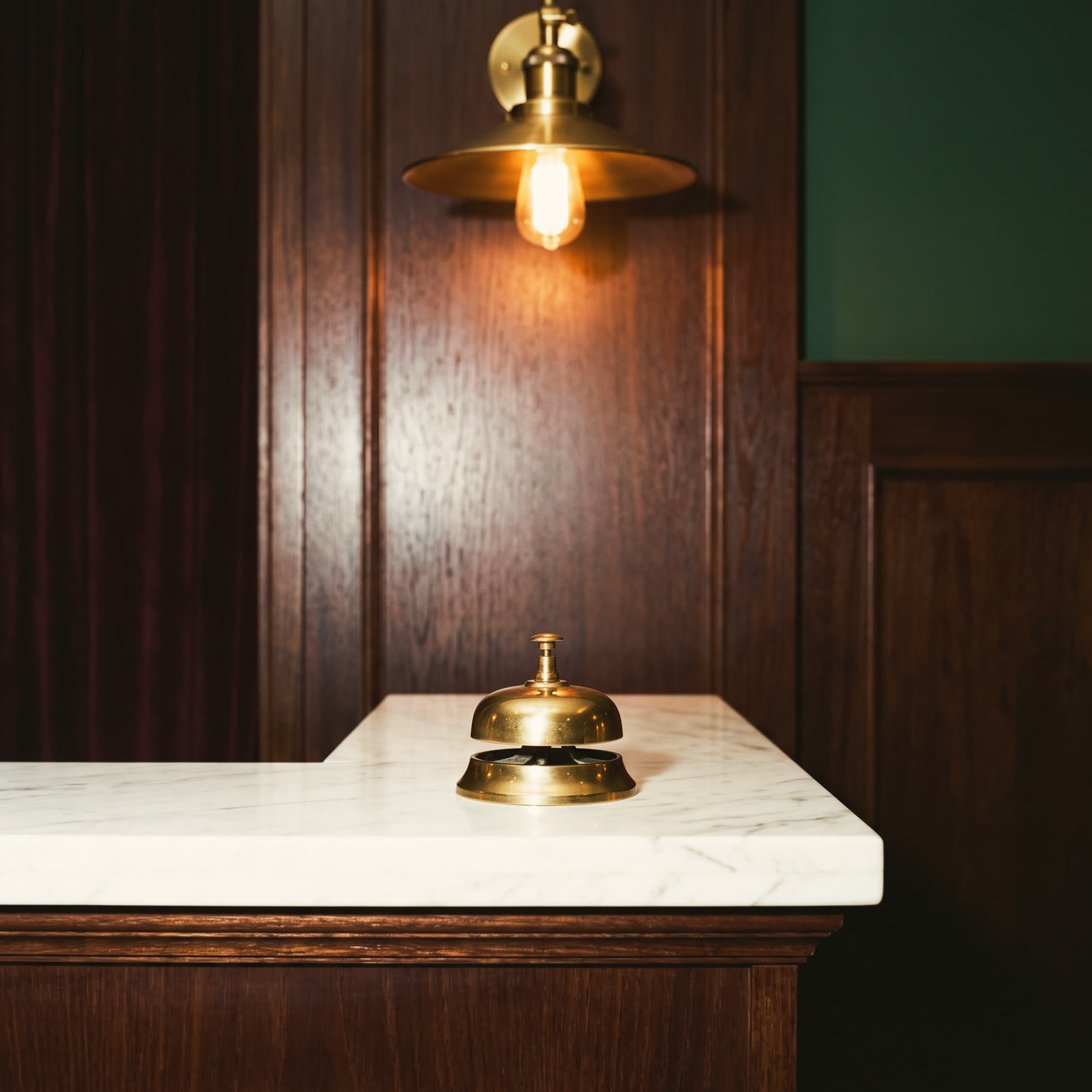 A brass reception bell on a marble counter under one lamp